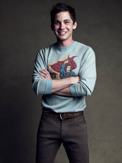 a man with his arms crossed standing in front of a gray background wearing a superman sweater
