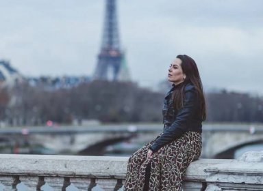 Woman with a bored expression sitting on a stone railing with the Eiffel Tower in the distance.