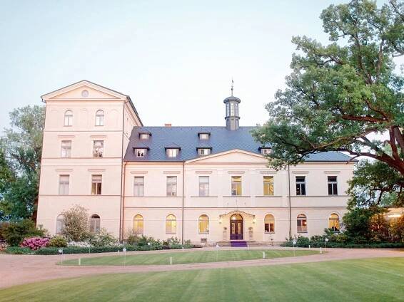Chateau Mcely, a spacious white mansion with a lush front lawn.