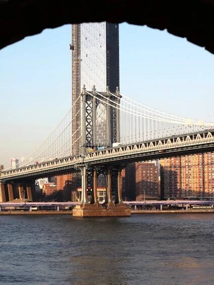 Image of the New York City skyline behind a suspension bridge.