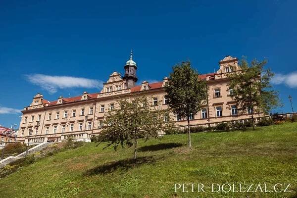 Vršovický zámeček vyfotografovaný z podhledu přes travnatý svah a stromy