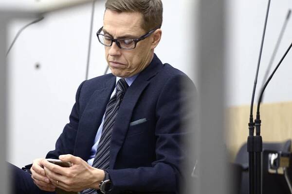 Vakavailmeinen valtiovarainministeri Alexander Stubb tutkii kännykkäänsä eduskunnassa.