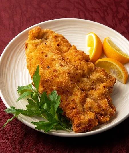two pieces of fried fish on a white plate with lemons and parsley next to it