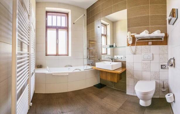 a bathroom with a tub and a toilet and a sink at Wellness & spa hotel Augustiniánský dům in Luhačovice