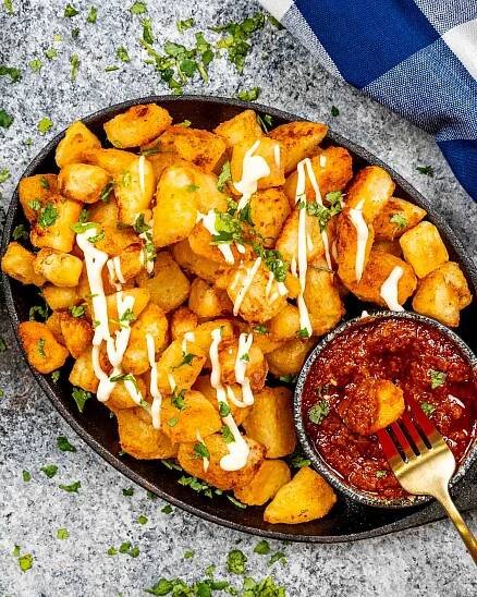 patatas bravas in an oval skillet with spicy red sauce.