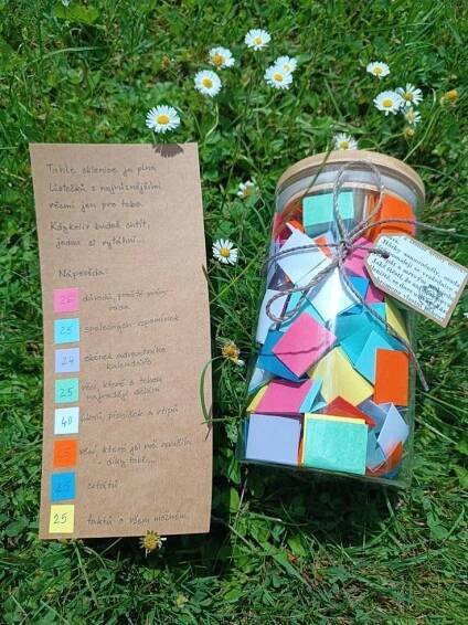 a jar filled with lots of different colored tiles next to a piece of paper on the ground