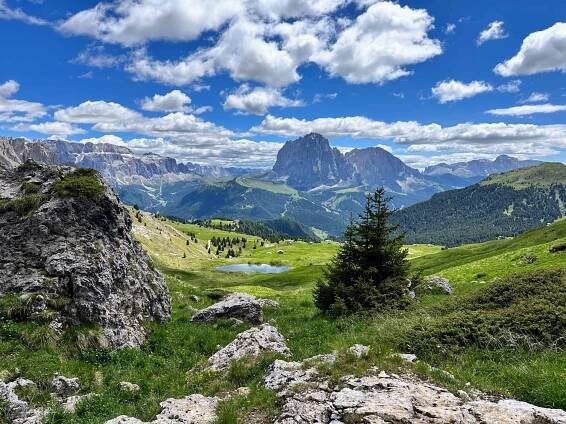View of small pond, green plateau, and mountains from the trail to Pieralongia in the Dolomites.