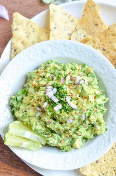 guacamole served in white bowl with chips and lime wedges at side.