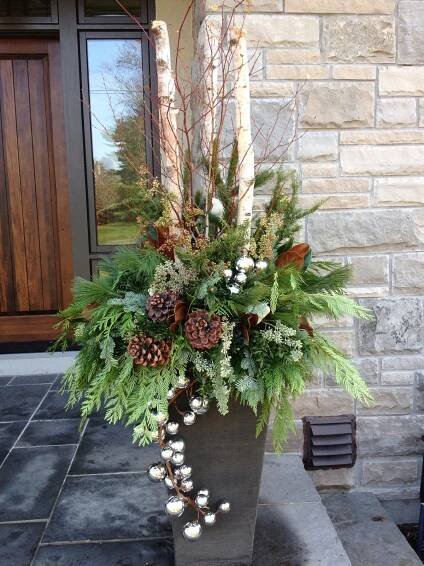 a tall planter filled with lots of greenery and pine cones on top of a stone walkway