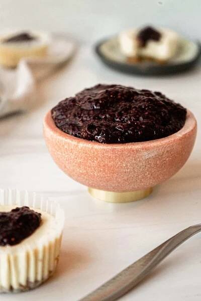 Light cheesecake recipe with cheesecakes scattered around the photo.  The focus is on a bowl of berry chia seed jam, which is a topping for the light cheesecake.