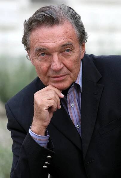 an older man in a suit and tie looking at the camera with his hand on his chin