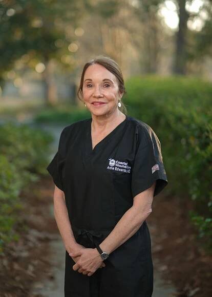 Healthcare professional in black scrubs standing outdoors on a pathway with trees and bokeh lighting in background.