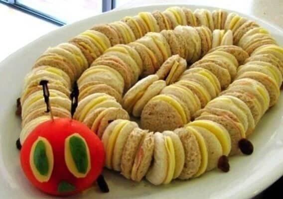 a white plate topped with sandwiches and a red apple next to a toy worm on top of it