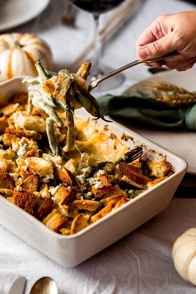 a woman serving up a spoonful of cheesy green bean casserole