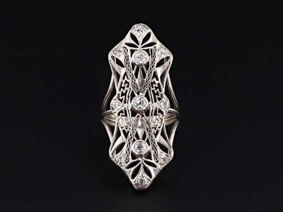 Art Deco Diamond Ring in 10K & 14K White Gold Converted from 1920s Brooch  Add a touch of antique glamour to your collection with this striking Art Deco diamond ring, skillfully transformed from a brooch dating to circa 1920-1930. Showcasing the bold geometry and refined sparkle typical of the era, the ring merges period authenticity with modern craftsmanship. The face of the ring is crafted in 10K white gold and features a dramatic arrangement of twelve glittering diamonds, set in an iconic Art 