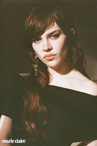 sophie thatcher posing with her bangs parted to the side and in a black off the shoulder dress