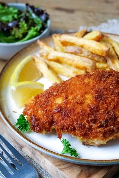 Hähnchen-Cordon-Bleu mit Pommes und Zitronenspalten auf einem Teller.