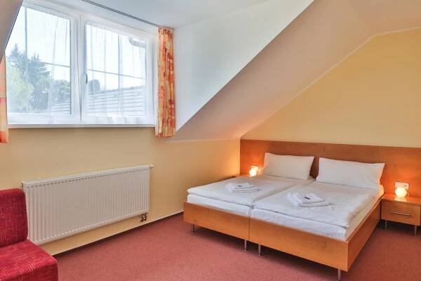 a small bedroom with a bed and a red chair at Hotel České Žleby in Stožec