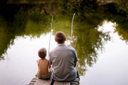 Dad and son fishing outdoors, view from back. Father and his son fishing together from wooden jetty on lake. Summertime, happy childhood. — Stock Image