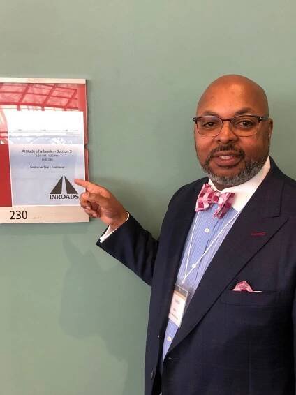 A man in a suit and tie is pointing at a sign on a wall.