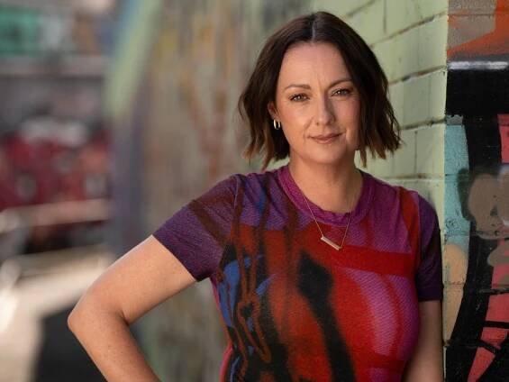 Celeste Barber leans against a grafitti wall, her hand on her hip, netural expression on her face