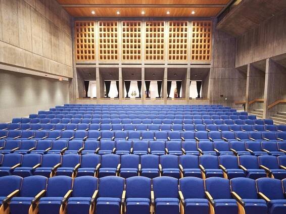 A photograph of the inside of the Everson's Hosmer Auditorium featuring 300 blue theater seats and the iconic stone grey walls.