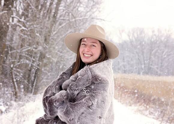 A winter portrait with someone wearing a beige hat and grey fur wrap in the snow.