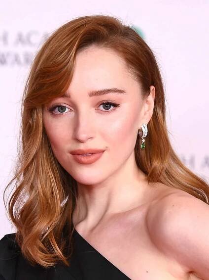 Phoebe Dynevor in a black one-shoulder dress with dark strawberry blonde hair