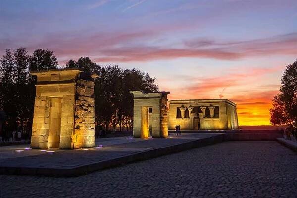 The Temple of Debod illuminated at sunset, with a stunning sky of pink and orange hues in the background.