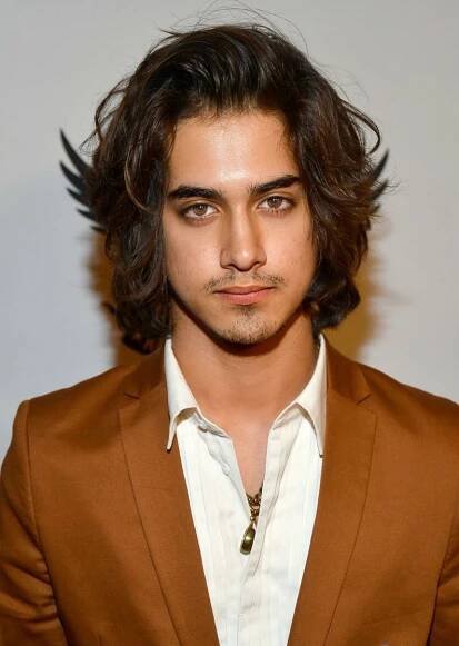 a man with long hair wearing a brown suit and white shirt is looking at the camera