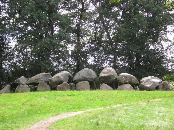 two rows of large boulders covered by other boulders in front of green trees; Dolmen D18 near Assen