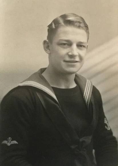 Boyish young man with short fair hair, wearing a sailor's tunic with a striped collar.