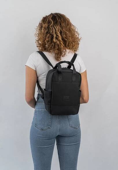 Černý batoh vyrobený z odolné tkaniny, s dvěma horními madly, nastavitelnými popruhy a minimalistickým designem s předním logem.