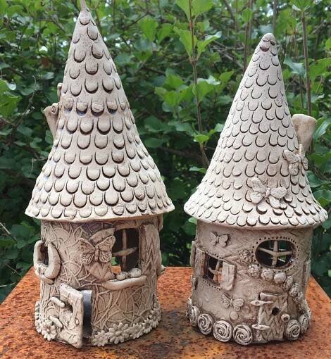 two clay houses sitting on top of a wooden table next to some trees and bushes
