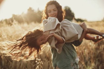 a young girl being spun around in a field with her mother