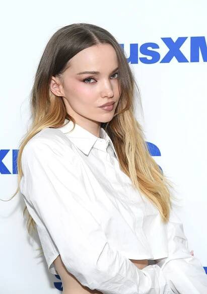 Person with long hair wearing a cropped white button-up shirt poses against a SiriusXM backdrop