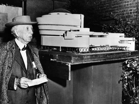 Black-and-white image of Frank Lloyd Wright standing beside his Guggenheim Museum model.