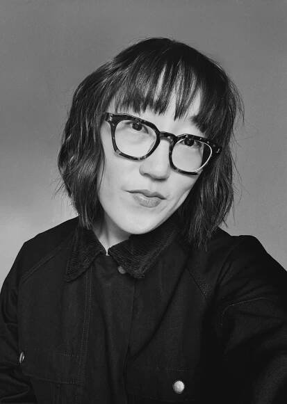 Sojin Rank, a Korean woman with short brown hair and bangs wearing large-framed glasses and a black jacket.