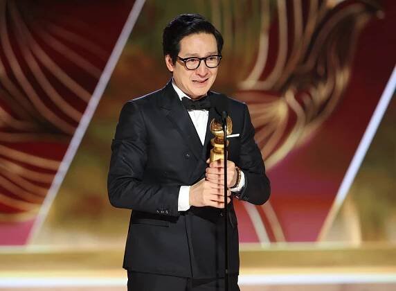 Ke Huy Quan stands at a microphone onstage and holds his Golden Globe.