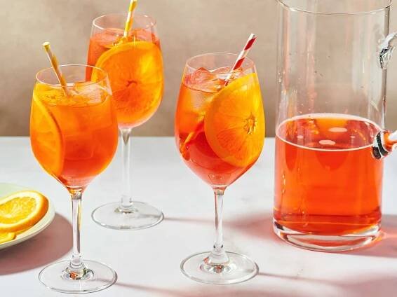 Glasses filled with Aperol Spritz garnished with orange slices, a pitcher of the drink is next to them