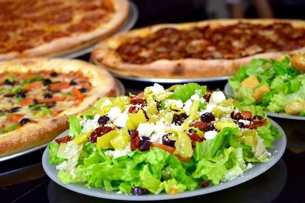A table topped with plates of pizza and salad.