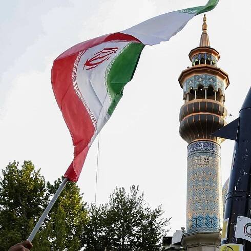 Iraner heben eine Flagge und die Attrappe einer Rakete während einer Feier nach dem iranischen Raketen- und Drohnenangriff auf Israel am 15. April 2024 auf dem Palästina-Platz im Zentrum von Teheran. 