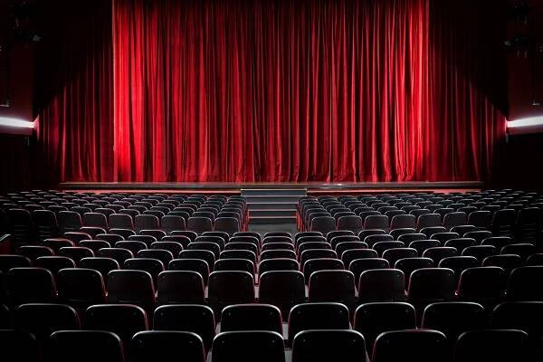 Interior view of The Arts Council Theatre showing rows of empty black seats facing a large closed red curtain on stage.