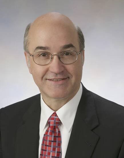 Doctor Newman is wearing a dark suit with a white shirt and patterned tie.