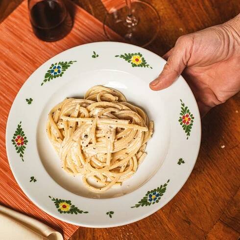 a hand sets down a bowl of handmade bucatini cacio e pepe