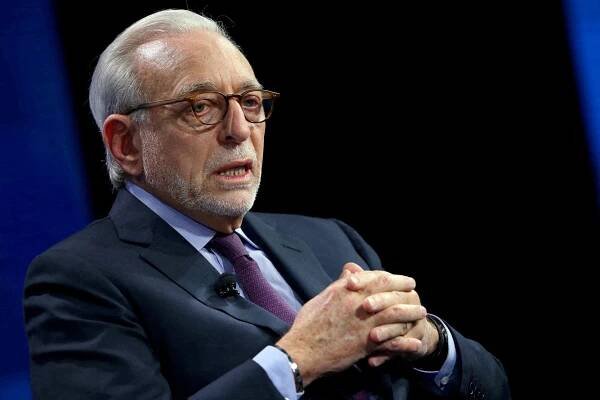 Nelson Peltz speaks while sitting on a stage with his hands folded in front of him.