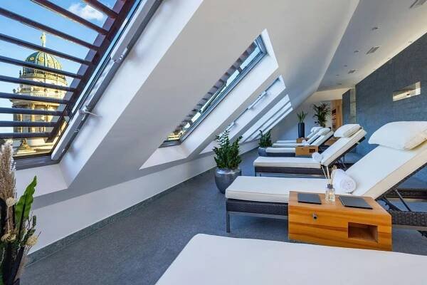 Hotel Luc, Autograph Collection Berlín Exteriér fotografie The photo shows a modern and serene spa room with several massage tables arranged in a row. The room has a high, angled ceiling with large skylights that let in natural light. The walls are painted a light gray, and one wall is covered in a textured 