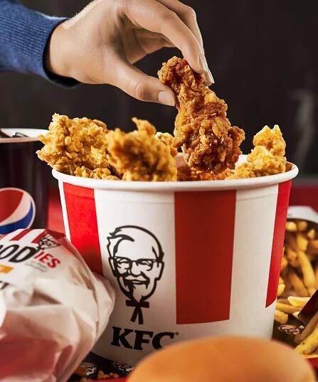eine Hand greift in einen rot-weißen Bucket gefüllt mit Chickenwings