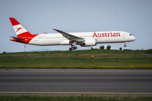 Flugzeuge der Austrian Airlines landen auf einer Landebahn mit grünem Gras und Bäumen im Hintergrund.