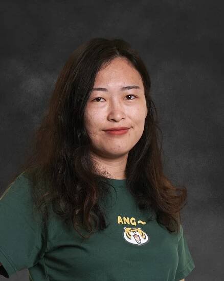 A woman in front of a gray background wearing a forest green shirt with a tiger emblem.